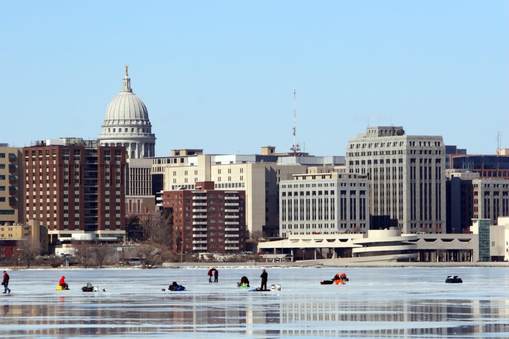 People ice fishing near city buildings in winter.