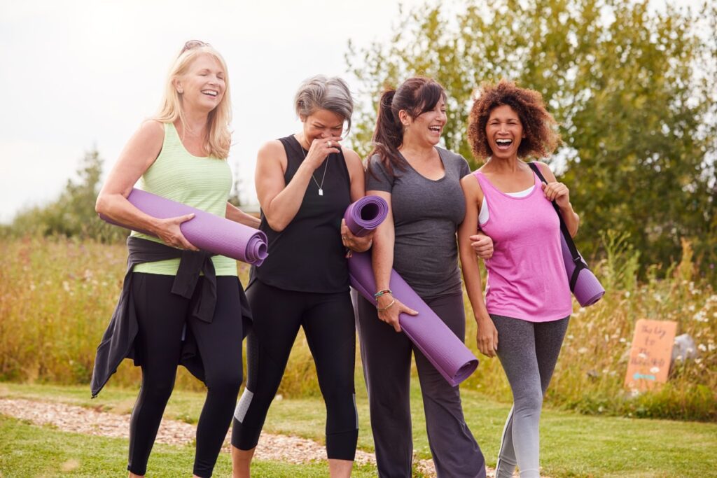 Group of women with yoga mats outdoors, laughing.