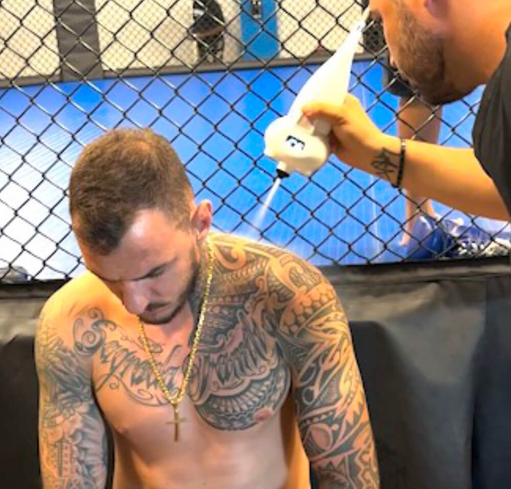 Tattooed fighter receiving treatment in gym.